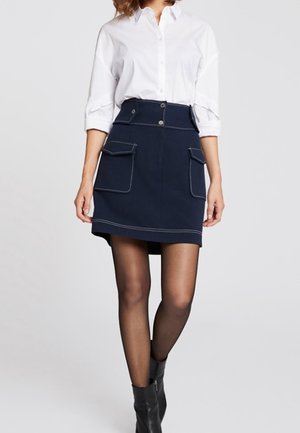 Námořnická sukně s dvěma předními klopovými kapsami, kontrastním šitím a vysokým pasem. V kombinaci s bílou košilí s knoflíky a černými kotníkovými botami.