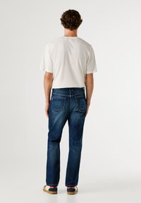 Bílá krátká trička s krátkým rukávem v kombinaci s tmavě modrými džíny. Džíny mají klasický střih a dvě zadní kapsy. Jednoduchý design, bez vzorů.