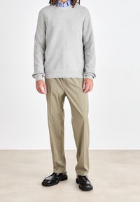 Ljust grå stickad tröja, beige klänningbyxor med framfäll, och svarta läderskor. Enkl design, avslappnad passform, släta texturer.