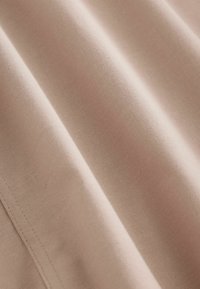 Světlý růžový textil s hladkým, matným povrchem; má jemnou strukturu a prošité okraje, vykazuje měkké záhyby a vrásky.