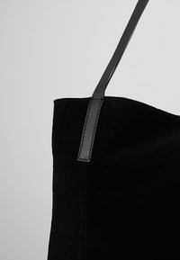 Czarna zamszowa torba na ramię z gładką skórzaną rączką, charakteryzująca się prostymi liniami i detalami w szwach oraz miękką teksturą.