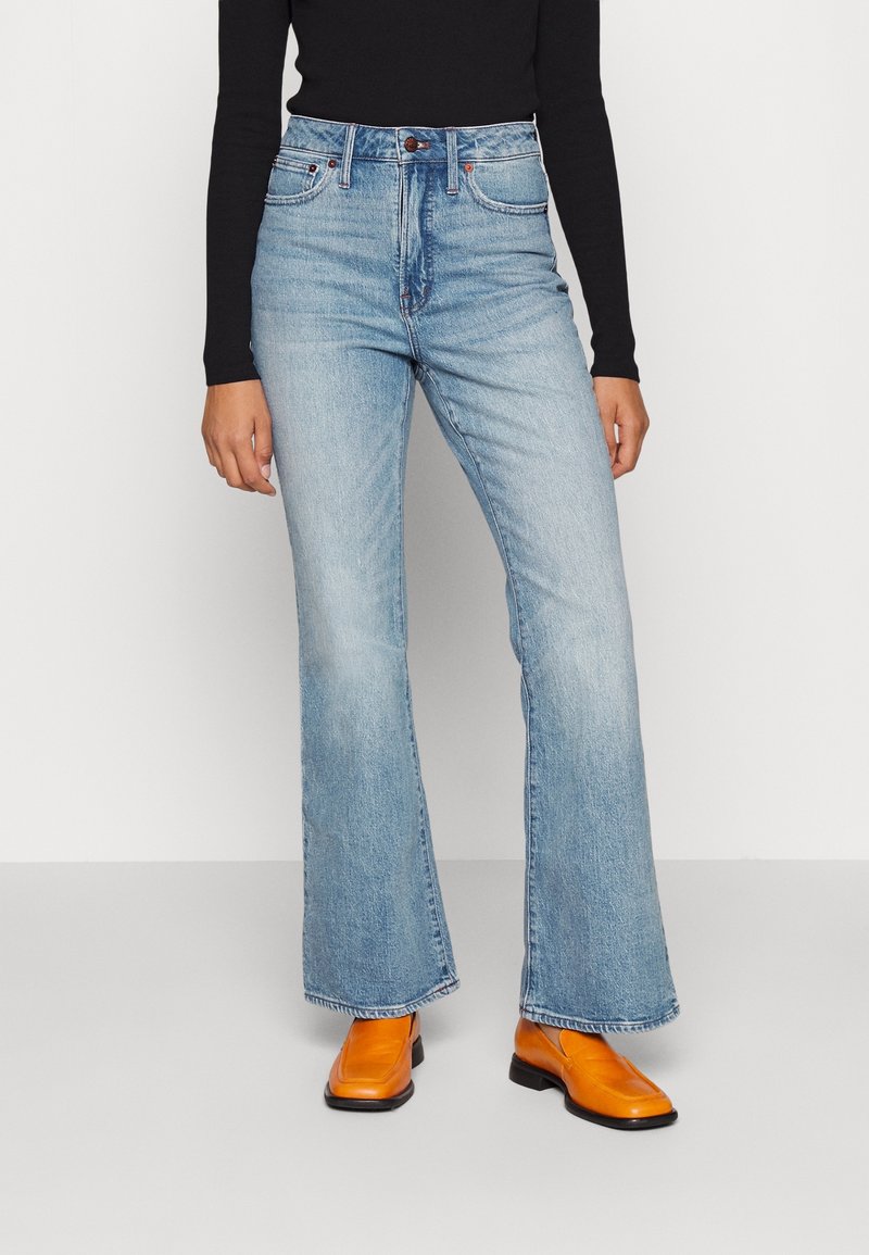 Jeans de mezclilla azul claro de corte acampanado con cintura alta, con un cierre frontal de botón y un diseño clásico de cinco bolsillos. Combinados con botas naranjas.