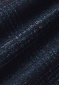Tkanina wełniana, ciemnoniebieska z subtelnymi szarymi i czerwonymi wzorami, fakturowana powierzchnia o miękkim, puszystym odczuciu, złożona i warstwowa.