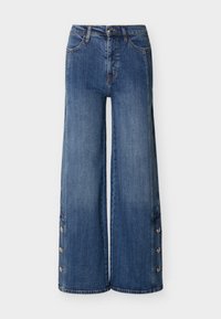 Μπλε τζιν ψηλόμεσο, με ευρύ μπατζάκι, κουμπιά στο εμπρόσθιο μέρος και κουμπιά πίεσης κατά μήκος των εξωτερικών πλευρών των ποδιών, εμφανίζονται σε απλό φόντο.