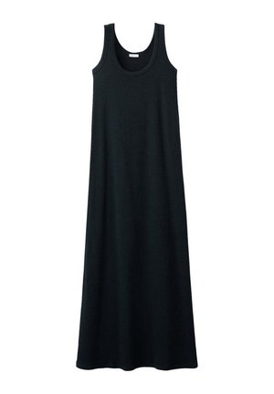 Femme en robe maxi noire sans manches tenant un grand sac panier tressé, portant des tongs, marchant devant un fond blanc uni.