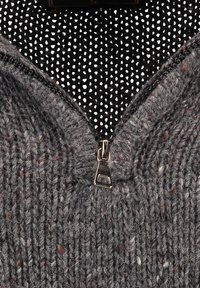 Grauer gestrickter Pullover aus strukturiertem Stoff, akzentuiert durch einen metallischen Reißverschluss am Hals und ein schwarzes gepunktetes Futter im Inneren.