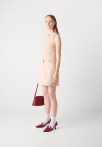 Débardeur beige à côtes associé à une mini-jupe beige avec une ceinture. Porté avec des chaussures à talons rouges et un sac à main rouge coordonné.