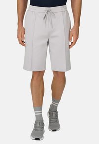 Hellgraue Sportshorts aus weichem Stoff, mit einem elastischen Bund mit Kordelzug und seitlichen Taschen. Kombiniert mit grauen Turnschuhen und Socken.