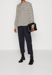 Long-sleeved, patterned blouse in black and cream, paired with dark navy trousers and sleek black ankle boots. Black handbag accent.