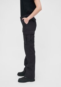 Svarte cargo-bukser med slim fit, med flere lommer, stikking detaljer og et robust stoff, kombinert med svarte sko.