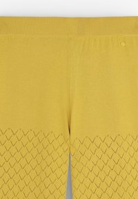 Leggings en tricot jaunes avec une taille côtelée et un motif de découpages en losange sur la partie inférieure. Texture lisse dans l'ensemble.