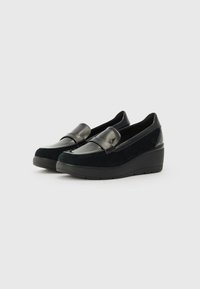 Mocassins noirs avec un talon compensé, présentant une combinaison de cuir lisse et de daim doux. Comprend une large sangle sur le dessus.