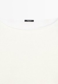 Vêtement blanc à col rond avec une petite étiquette noire cousue à l'intérieur du col indiquant « Massimo Dutti Made in China ».