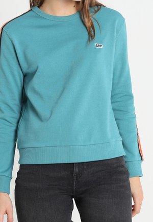 Sweatshirt bleu clair à col rond avec des poignets et un ourlet en côte ; présente des rayures latérales orange et un petit logo "Lee" sur la poitrine.
