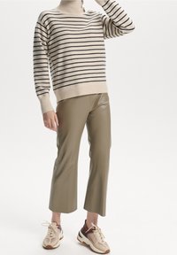 Suéter a rayas beige con cuello alto y detalle de botones, combinado con pantalones acampanados verde oliva y zapatillas beige con detalles marrones.