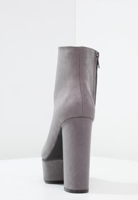 Šedá semišová kotníková obuv s vysokým blokovým podpatkem a zapínáním na zip na zadní straně. Hladký povrch s minimalistickým designem.