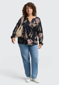 Blouse à manches longues bleu marine avec un imprimé floral rose et jaune, associée à un jean droit bleu clair et des baskets blanches. Portant un sac beige.