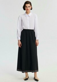 Cămășă albă cu mâneci lungi, asortată cu o fustă maxi neagră, dotată cu broderie florală colorată la margine. Design simplu și structurat.