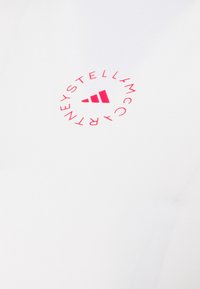 Bílý textil s kulatým logem v jasně růžové barvě, na kterém jsou napsaná slova "STELLA McCARTNEY" a uprostřed tři nahoře postavené trojúhelníky.