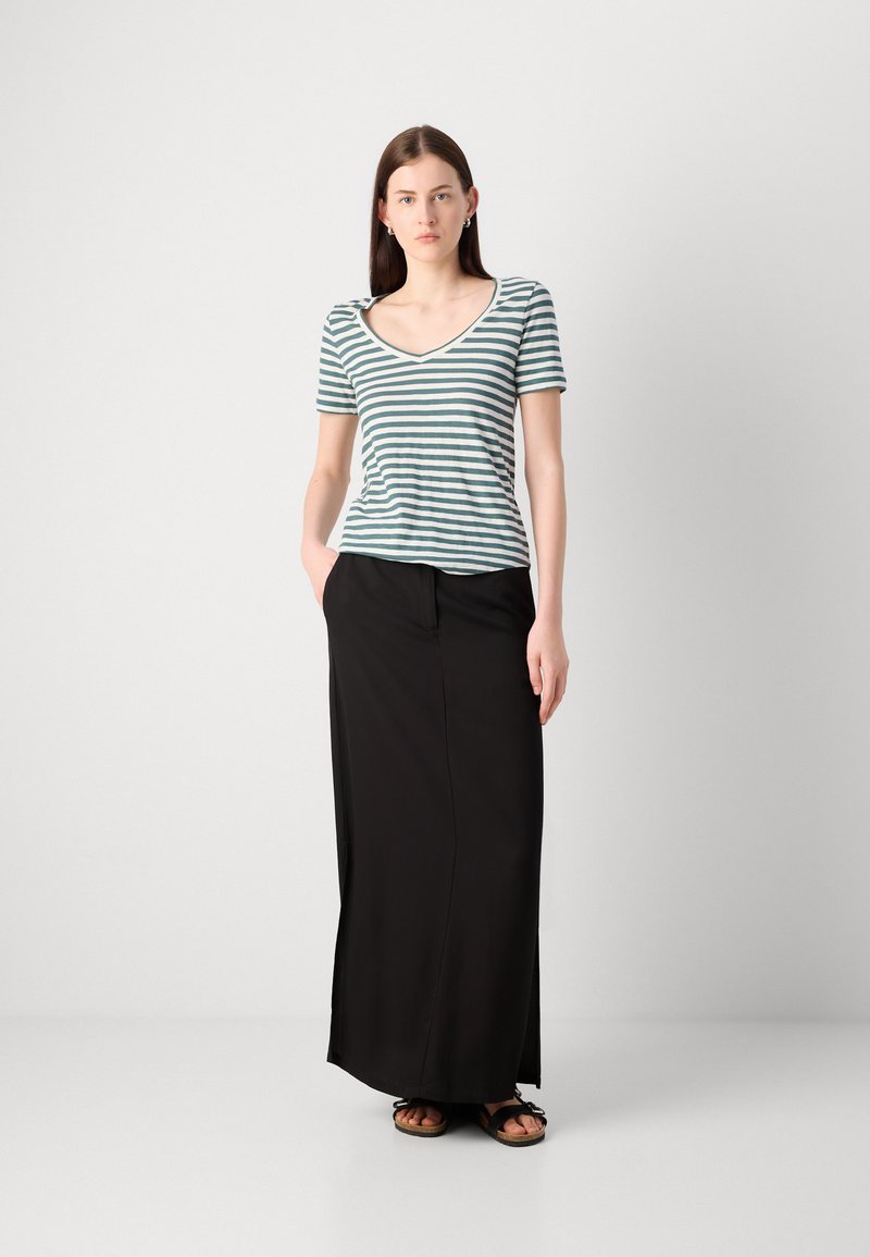 Pasiasty t-shirt w kolorze turkusowym i białym z dekoltem w serek oraz krótkimi rękawami, zestawiony z długą czarną spódnicą. Ubranie charakteryzuje się luźnym krojem i kieszeniami.