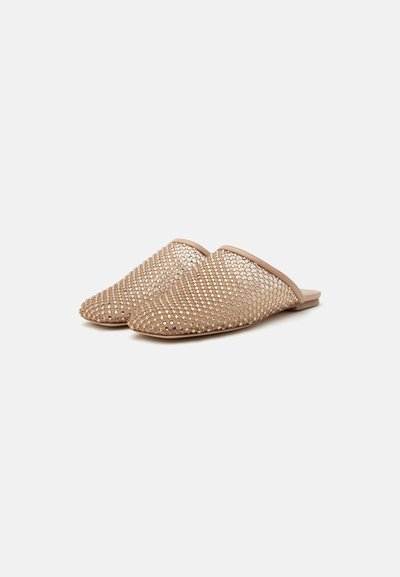 Mules plates beige à enfiler avec bouts pointus, recouvertes d'un motif de petits clous métalliques sur un fond uni.