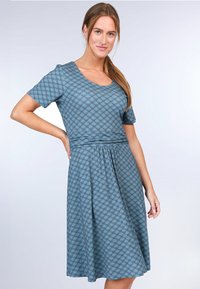 Ein kurzärmliges Kleid in Tealfarbe mit einem Blättermuster, das einen Rundhalsausschnitt und eine taillierte Taille aufweist, die in einen plissierten Rock übergeht.