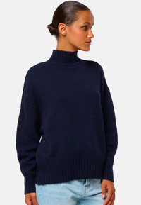 Pull en tricot bleu marine avec un col montant, des manches larges et un ourlet côtelé. Texture douce, coupe décontractée, idéal pour le superposition.