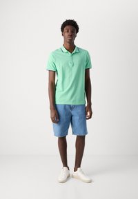 Polo de algodón verde con ribetes negros, combinado con shorts de mezclilla azul claro y zapatillas blancas. Diseño simple con cierre de botones.