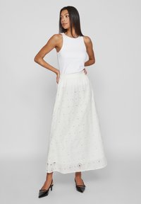 Λευκή, κεντημένη μάξι φούστα με υφασμάτινο μοτίβο και ελαστική μέση. Συνδυάζεται με μια εφαρμοστή, αμάνικη λευκή μπλούζα και μαύρες ψηλές γόβες.