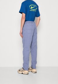 Blå t-shirt med neonsymbol, bärs tillsammans med ljuslila tapered cargo-byxor med fickor, och beige sneakers med mörka accenter.