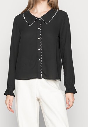 Chemise noire à boutons avec col festonné et patte de boutonnage. Manches longues avec poignets à volants ; tissu léger. Accents blancs tout au long.