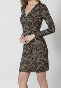 Sukienka z długim rękawem o asymetrycznym kroju, z kwiatowym wzorem w kolorze czerwonym, żółtym i białym na czarnym tle, o dopasowanym fasonie.