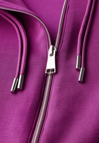 Fuchsiasfärgad zip-up jacka med silverfärgad dragkedja, med mjukt tyg och kontrasterande dragskoändar i cylindrisk form.