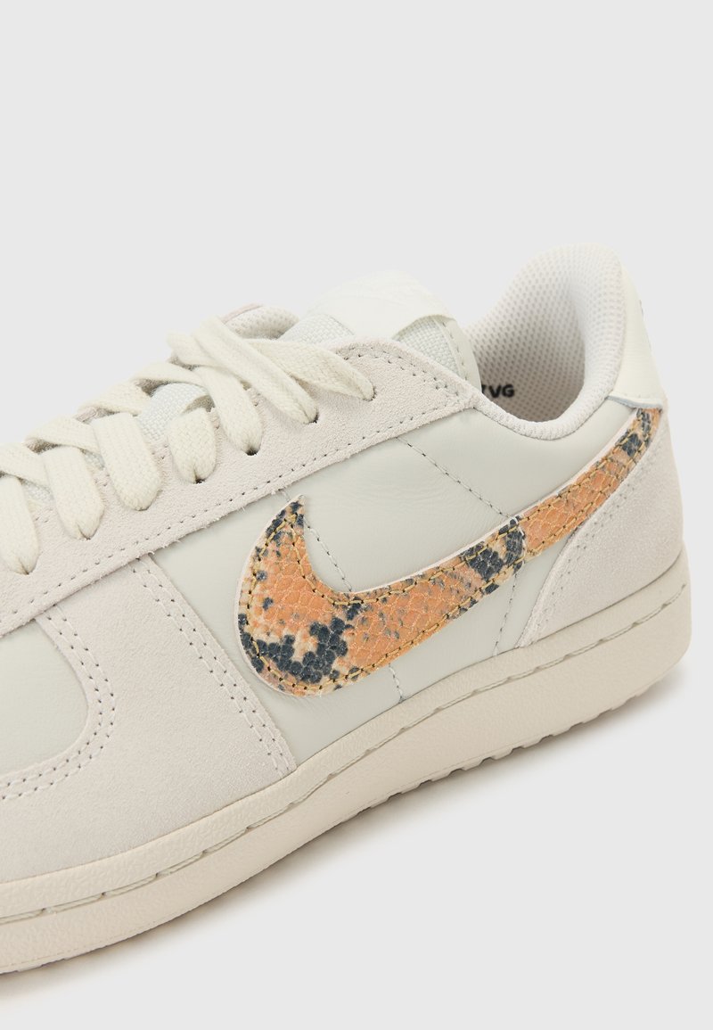 Baskets Nike avec un dessus en cuir et daim gris clair. Comprend un motif serpent texturé orange et noir sur le logo Swoosh.