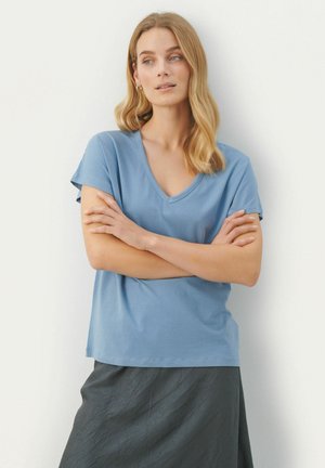 Blaues Baumwoll-T-Shirt mit V-Ausschnitt und kurzen Ärmeln, kombiniert mit einem strukturierten dunklen Rock. Einfaches Design, weicher Stoff und lockere Passform.