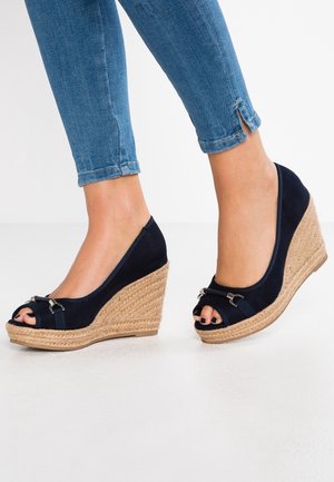 Marineblå kilehæle med åben tådesign, tekstiloverdel, rebindhylset hæl og metalliske detaljer på stroppen.