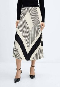 Gonna midi plissettata in crema e nero, caratterizzata da motivi geometrici con strisce diagonali. Indossata con scarpe col tacco nere.