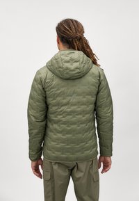 Zeleni, kviltani puffer jakna s kapuljačom, koja ima teksturirani uzorak, zatvaranje na zip i elastične manžete za toplinu i udobnost.