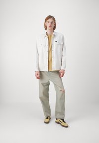 Camisa overshirt de denim blanco, camiseta amarilla, jeans claros con efecto desgastado y zapatillas amarillas con rayas negras. Diseño minimalista, corte casual.