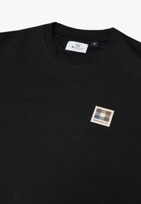 T-shirt nera in cotone con scollatura rotonda e un piccolo logo quadrato con un design a scacchi nei colori blu, grigio e beige sul davanti.