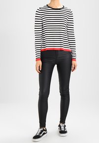 Gestreepte zwart-witte langemouwen top met een rode zoom, gecombineerd met zwarte slim-fit broek en zwart-witte sneakers.