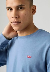 Jasnoniebieska koszula z długim rękawem z okrągłym dekoltem i małym logo Levi's w kolorze czerwonym na lewym piersi. Wykonana z miękkiej bawełny.