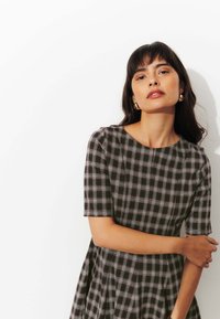 Robe à carreaux noir et blanc avec des manches courtes, un col rond et des détails de jupe plissée. Texture lisse et silhouette cintrée.