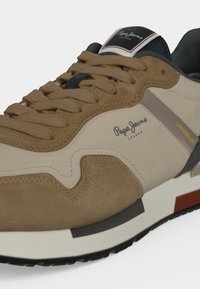 Κοντινή εικόνα ενός μπεζ και καφέ sneaker Pepe Jeans με σουέντ και υφασμάτινα υλικά, που δείχνει κορδόνια, λογότυπο και λεπτομέρειες μαύρης σόλας.