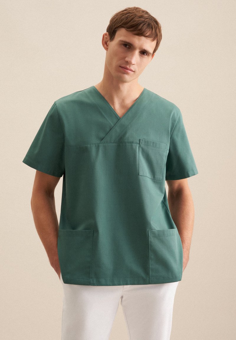 Tunique verte à col en V, à manches courtes et avec deux poches avant. Fabriquée en tissu doux avec une texture uniformes.