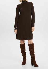 Abito in maglia marrone con collo a dolcevita, maniche lunghe e vestibilità comoda, abbinato a stivali alti in suede marrone con tacco a blocco.