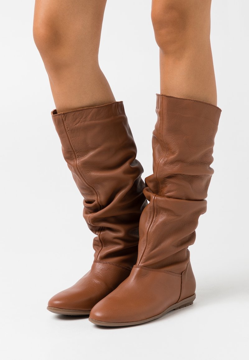 Bottes hautes marron en cuir avec un design décontracté, texture lisse, bout arrondi et semelle plate. Comprend une couverture de la cheville et des détails plissés.