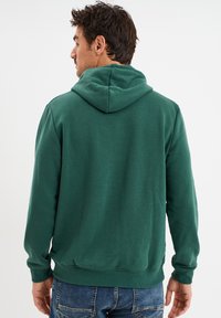 Felpa verde con cappuccio realizzata in morbido tessuto, con maniche lunghe, tasca a marsupio e polsini e orlo a coste.