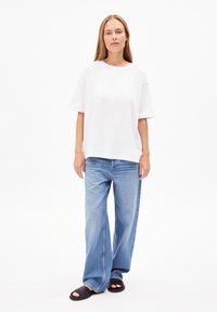 Weißes, übergroßes T-Shirt, lockere blaue Jeans mit ausgewaschenem Look und schwarze Sandalen. Einfaches, lässiges Outfit mit lockerer Passform.