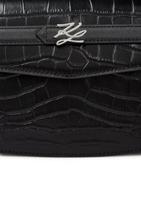 Black leather handbag with a textured crocodile pattern, featuring a silver logo accent and a flap closure.